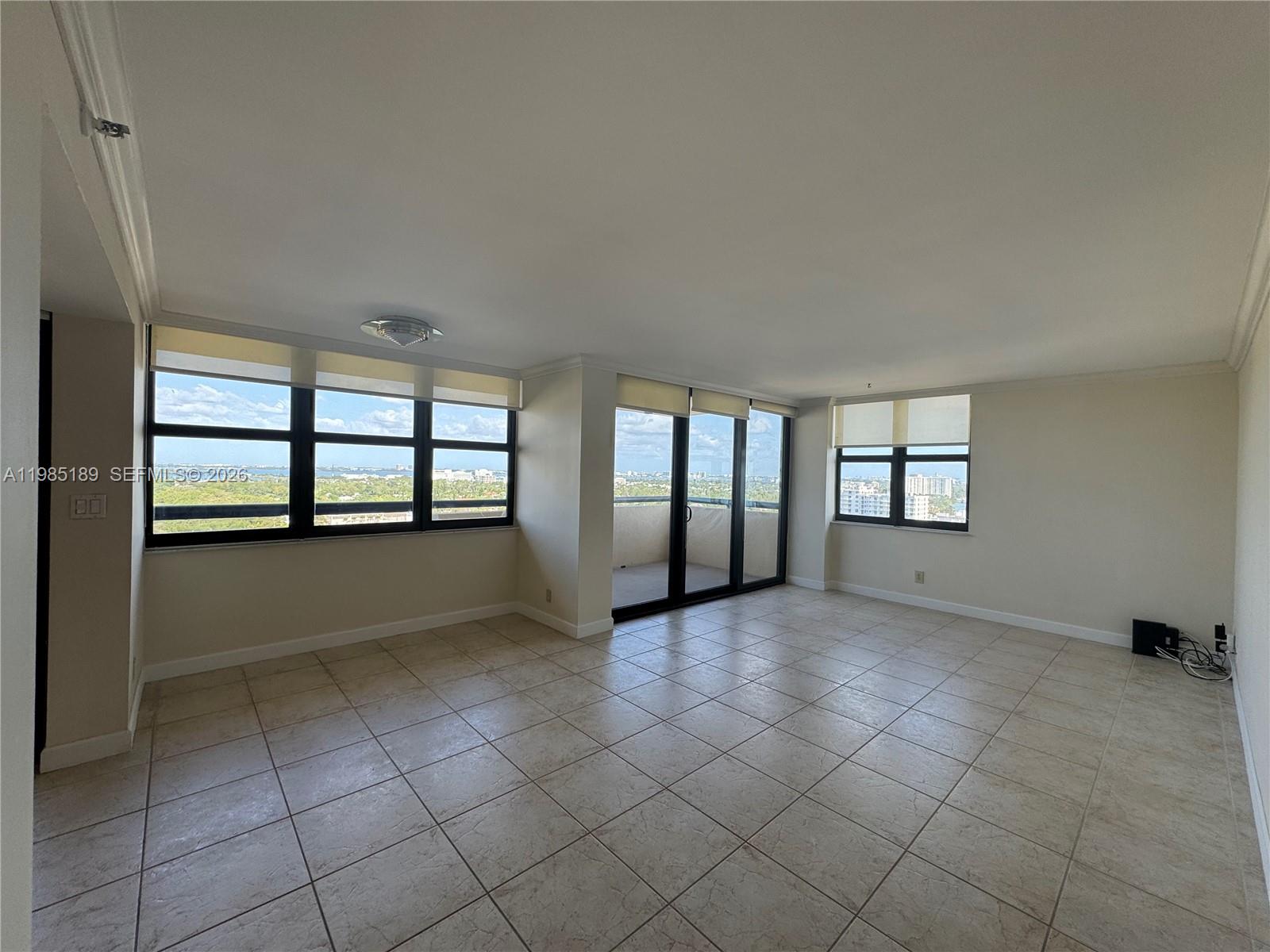 An empty living room features beige tile flooring, large windows, and a balcony entrance — 2555 Collins Ave # 2002, Miami Beach FL 33140, MIAMI BEACH, FL
