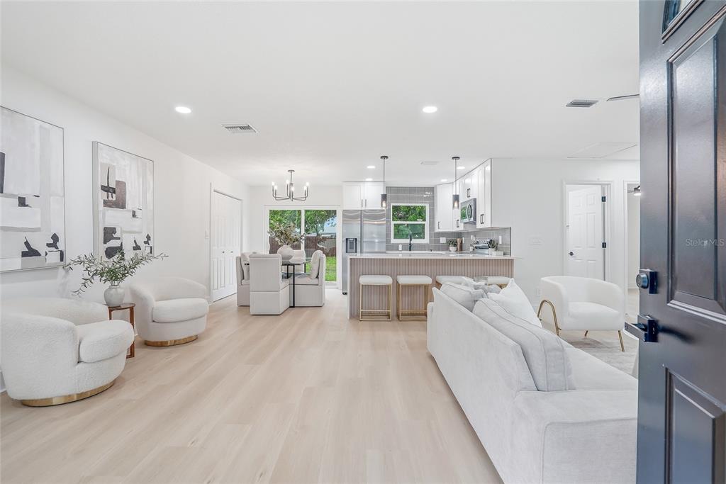 An open-concept living and dining area features white furniture, light wood flooring, and a kitchen — 6197 98TH AVENUE N, PINELLAS PARK, FL