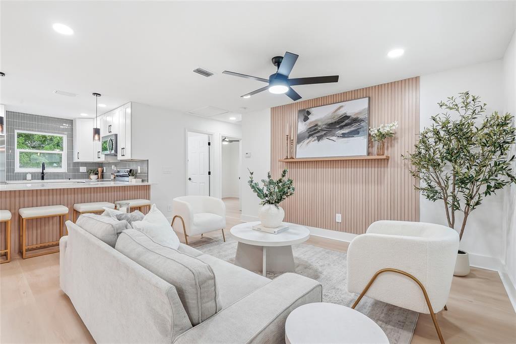 A living room features a slatted wood accent wall, white armchairs, and a kitchen island — 6197 98TH AVENUE N, PINELLAS PARK, FL