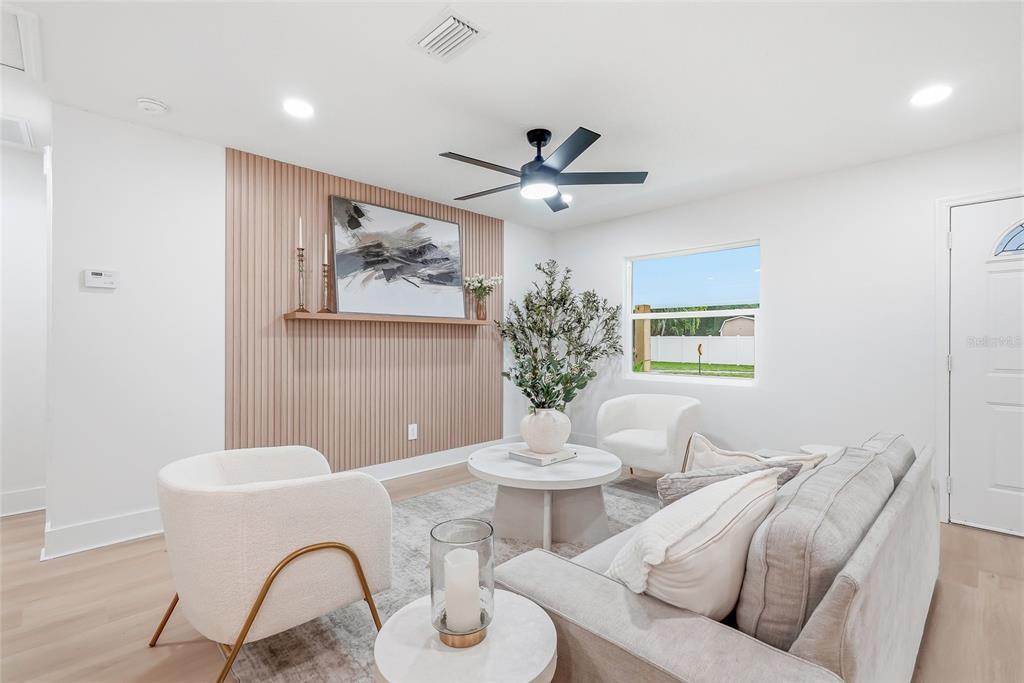 A living room features a slatted wood accent wall, white furniture, and a ceiling fan — 6197 98TH AVENUE N, PINELLAS PARK, FL