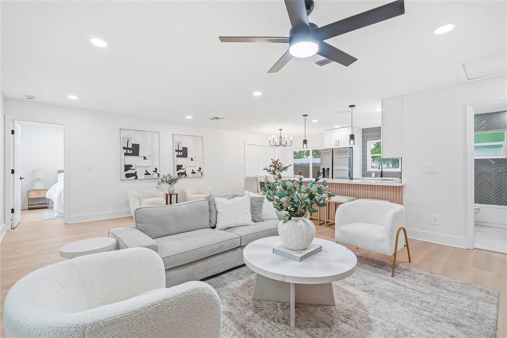 A bright, open-concept living room and kitchen featuring light wood floors and modern neutral furnishings — 6197 98TH AVENUE N, PINELLAS PARK, FL