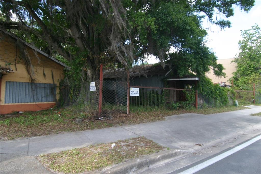 An overgrown, dilapidated house sits behind a chain-link fence on a sidewalk-lined street — 2720 OLD WINTER GARDEN ROAD, ORLANDO, FL