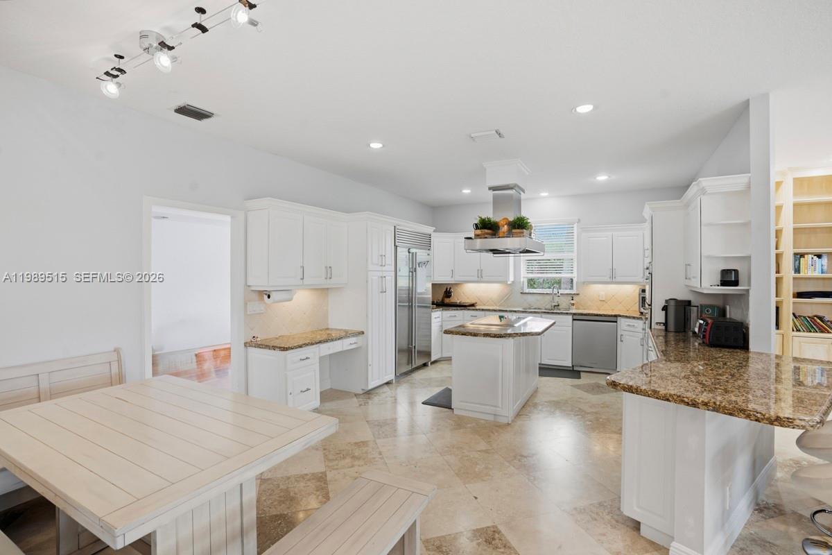 A white kitchen features granite countertops, a central island, and a dining area — 8179 Lakeview Dr, West Palm Beach FL 33412, WEST PALM BEACH, FL