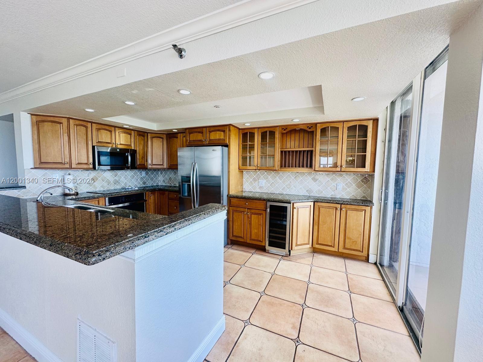 A kitchen with wood cabinets, granite countertops, stainless steel appliances, and tile flooring — 2555 Collins Ave # 711, Miami Beach FL 33140, MIAMI BEACH, FL