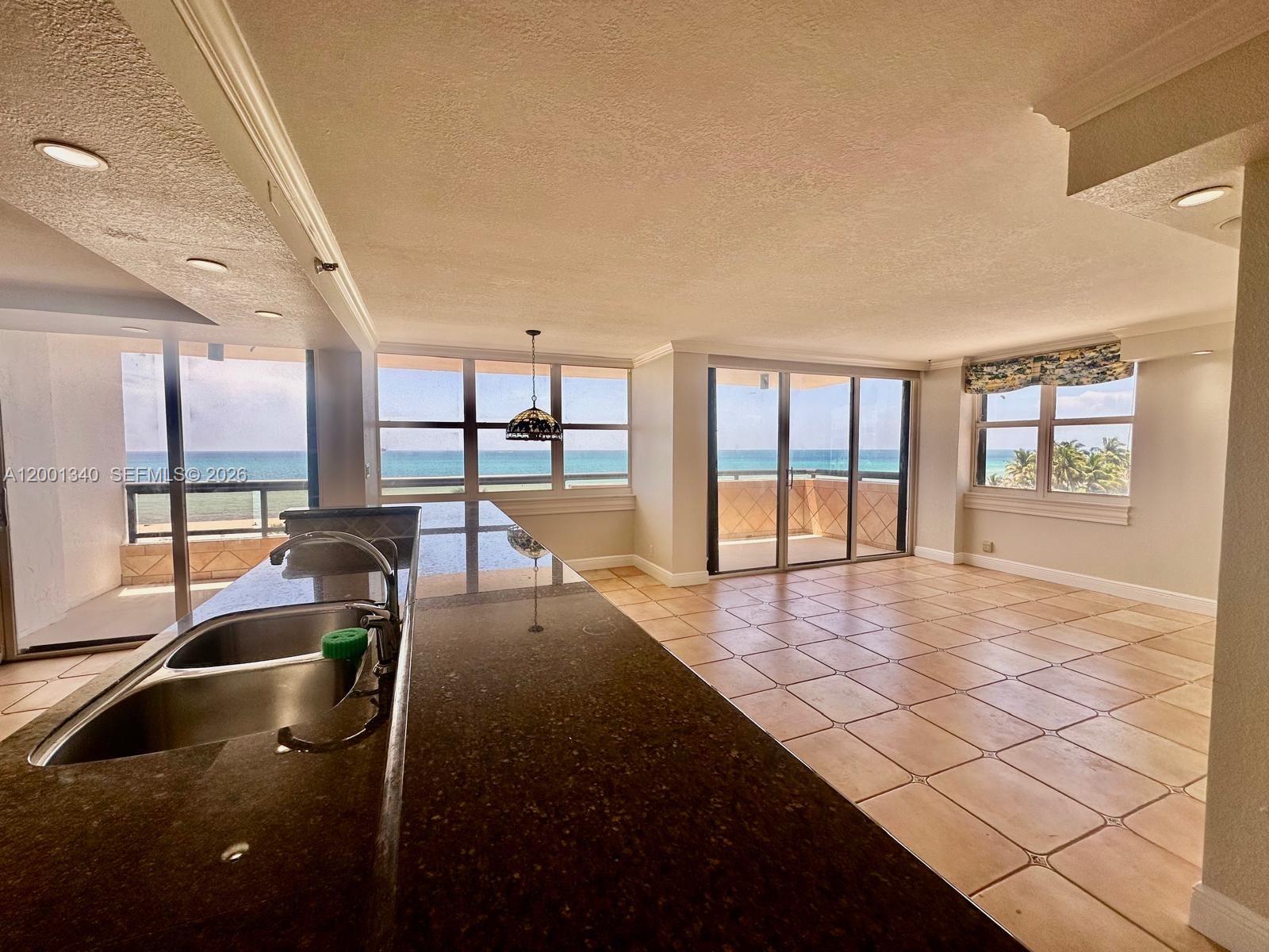 A kitchen with a dark countertop overlooks a living area with tile floors and ocean views — 2555 Collins Ave # 711, Miami Beach FL 33140, MIAMI BEACH, FL