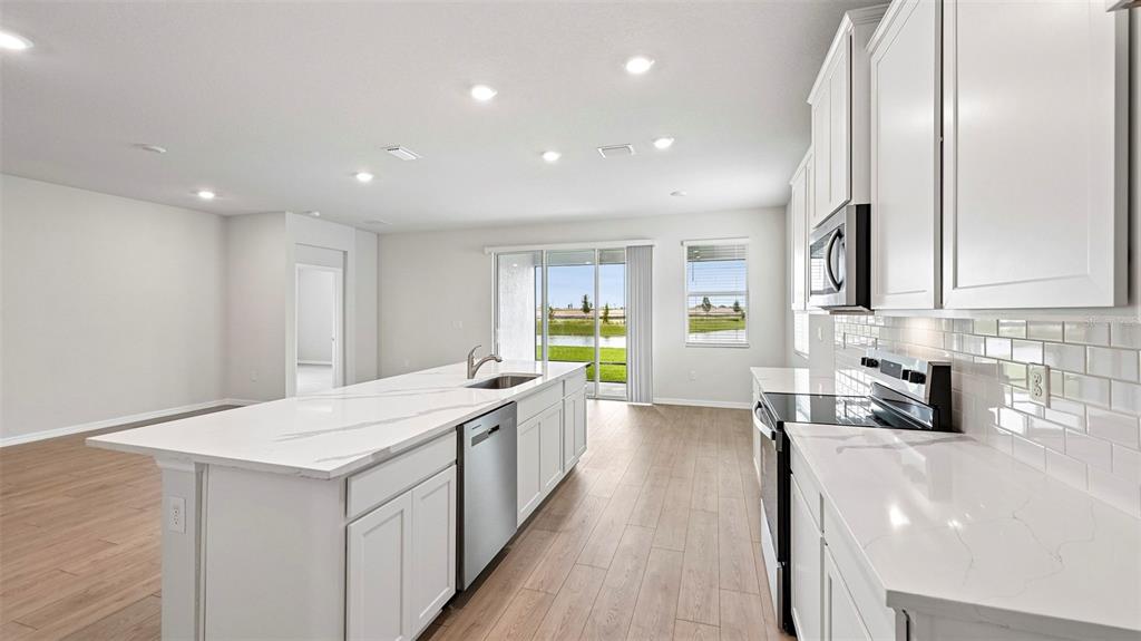 A modern kitchen features white cabinets, quartz countertops, stainless steel appliances, and light wood flooring — 17309 SALTBUSH TRAIL, PARRISH, FL