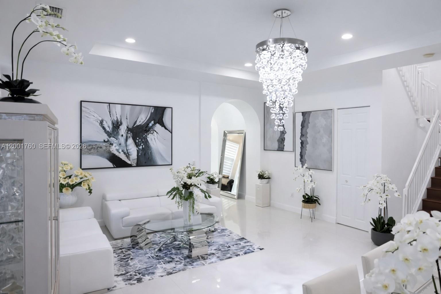 A bright, modern living room features white furniture, a crystal chandelier, and abstract wall art — 8537 NW 39th Ct, Cooper City FL 33024, COOPER CITY, FL