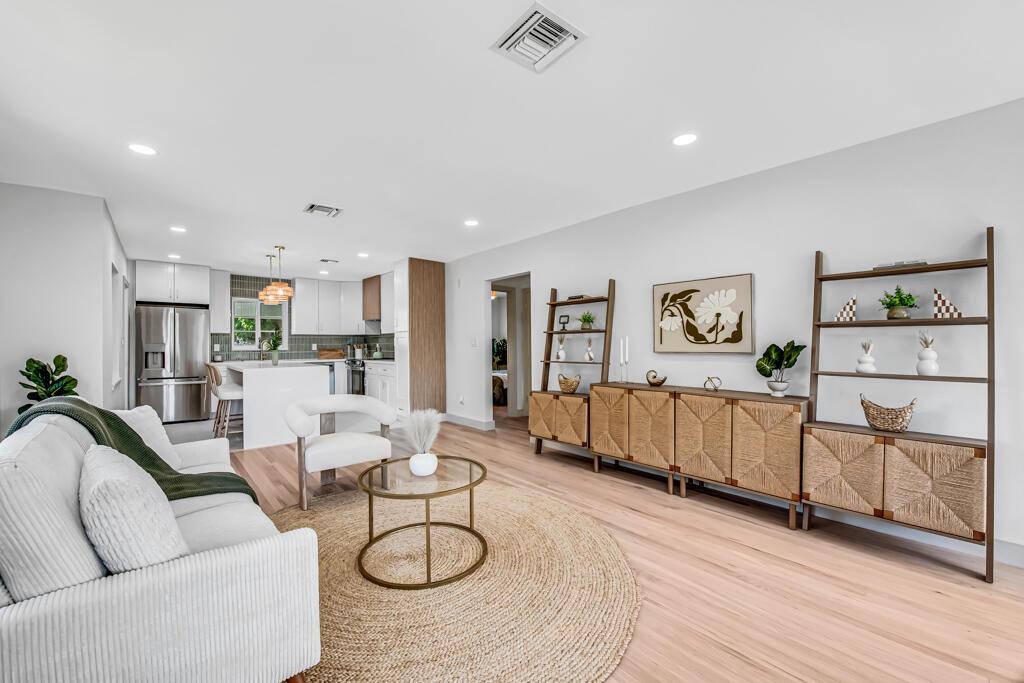 A bright open-concept living room and kitchen featuring light wood floors and modern white cabinetry — 1201 N Palmway, FL 33460, FL
