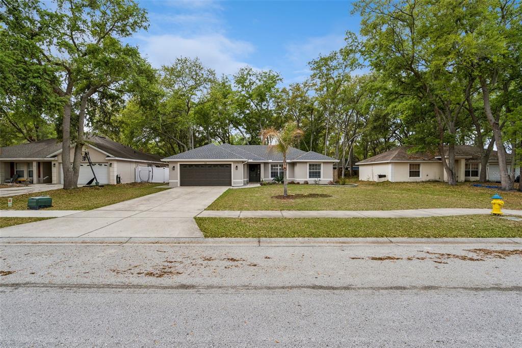 A single-story house with a brown garage door sits on a lawn with mature trees — 165 QUAIL OAKS CIRCLE, GROVELAND, FL