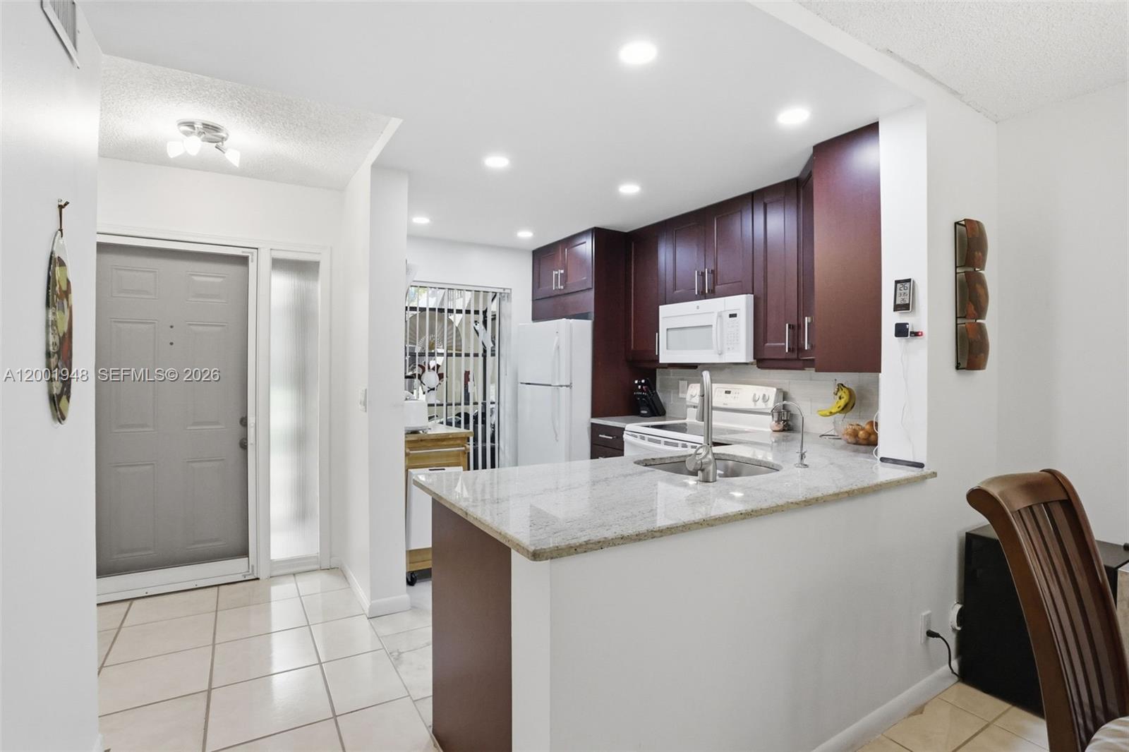A kitchen features dark wood cabinets, a granite countertop, and a white refrigerator — 2225 SW 15th St # 223, Deerfield Beach FL 33442, DEERFIELD BEACH, FL