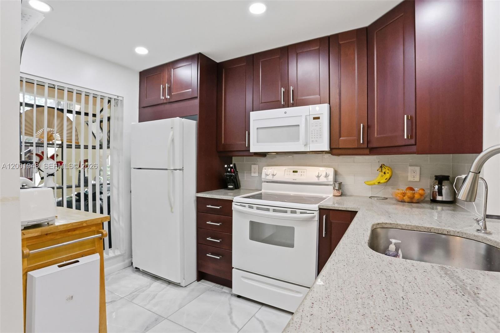 A kitchen features dark wood cabinets, white appliances, granite countertops, and light tile flooring — 2225 SW 15th St # 223, Deerfield Beach FL 33442, DEERFIELD BEACH, FL