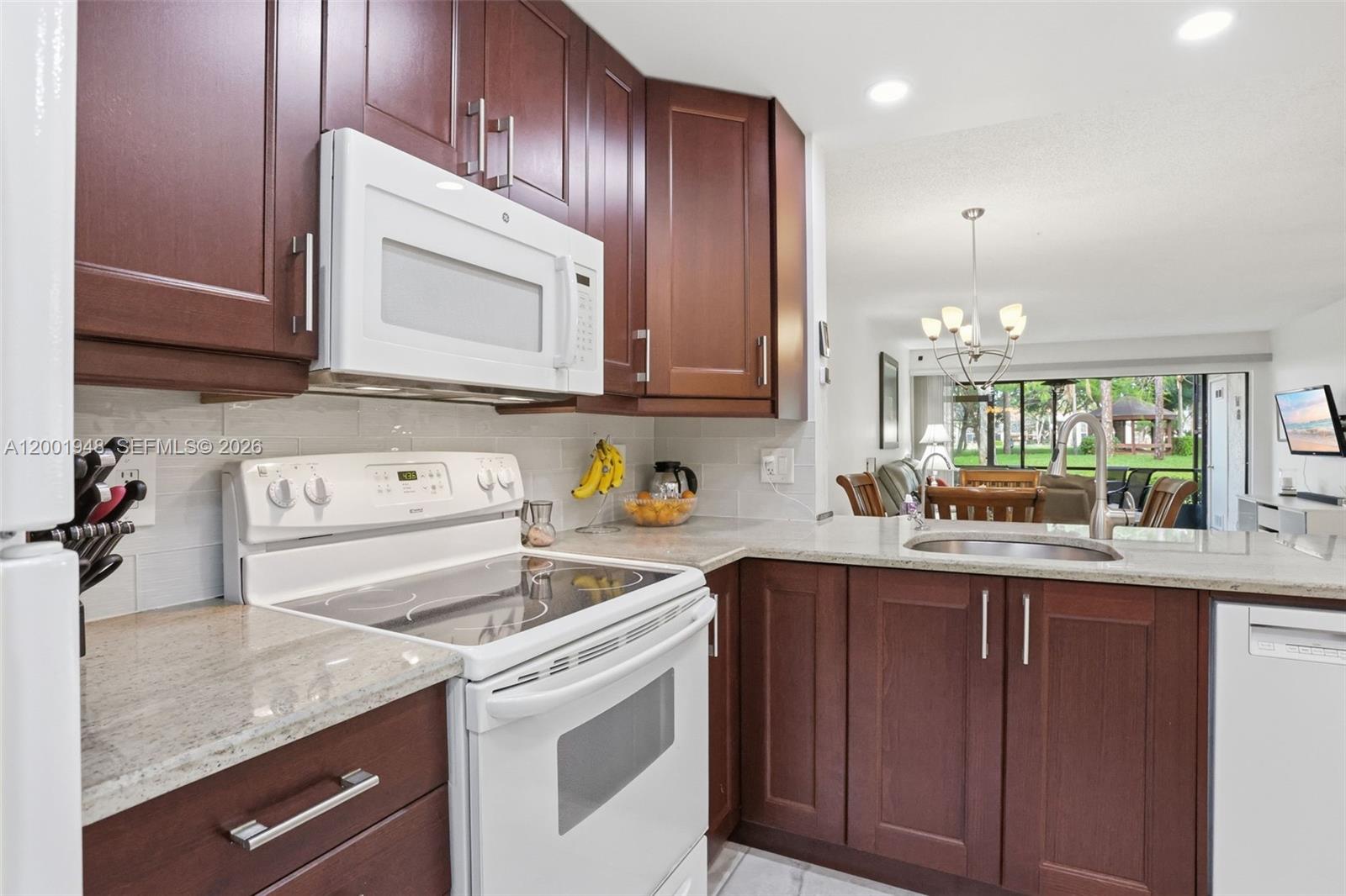 A kitchen features dark wood cabinets, white appliances, granite countertops, and an open dining area — 2225 SW 15th St # 223, Deerfield Beach FL 33442, DEERFIELD BEACH, FL