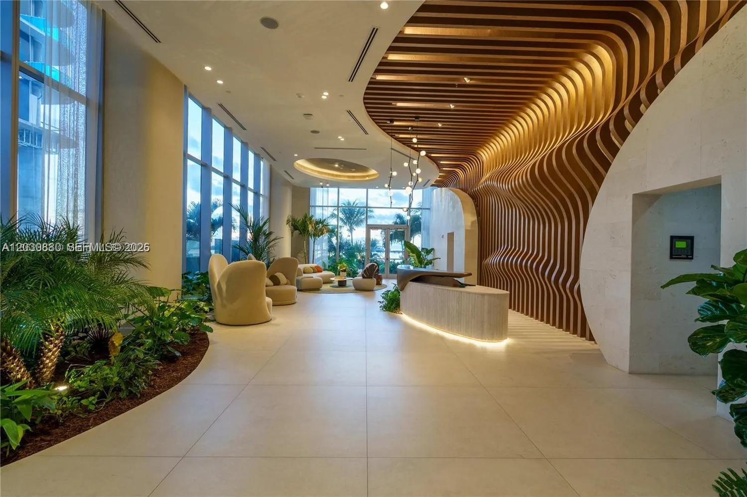 A modern lobby features a curved wood-slat ceiling, a stone reception desk, and floor-to-ceiling windows — 700 NE 24th St # 3502, Miami FL 33137, MIAMI, FL