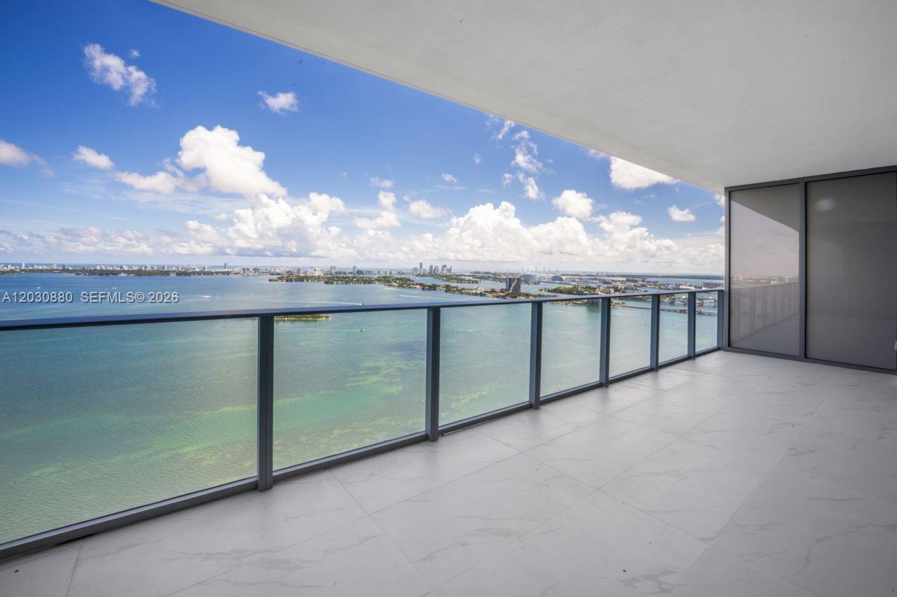 A high-rise balcony features glass railings and light-colored tile flooring overlooking a bay — 700 NE 24th St # 3502, Miami FL 33137, MIAMI, FL