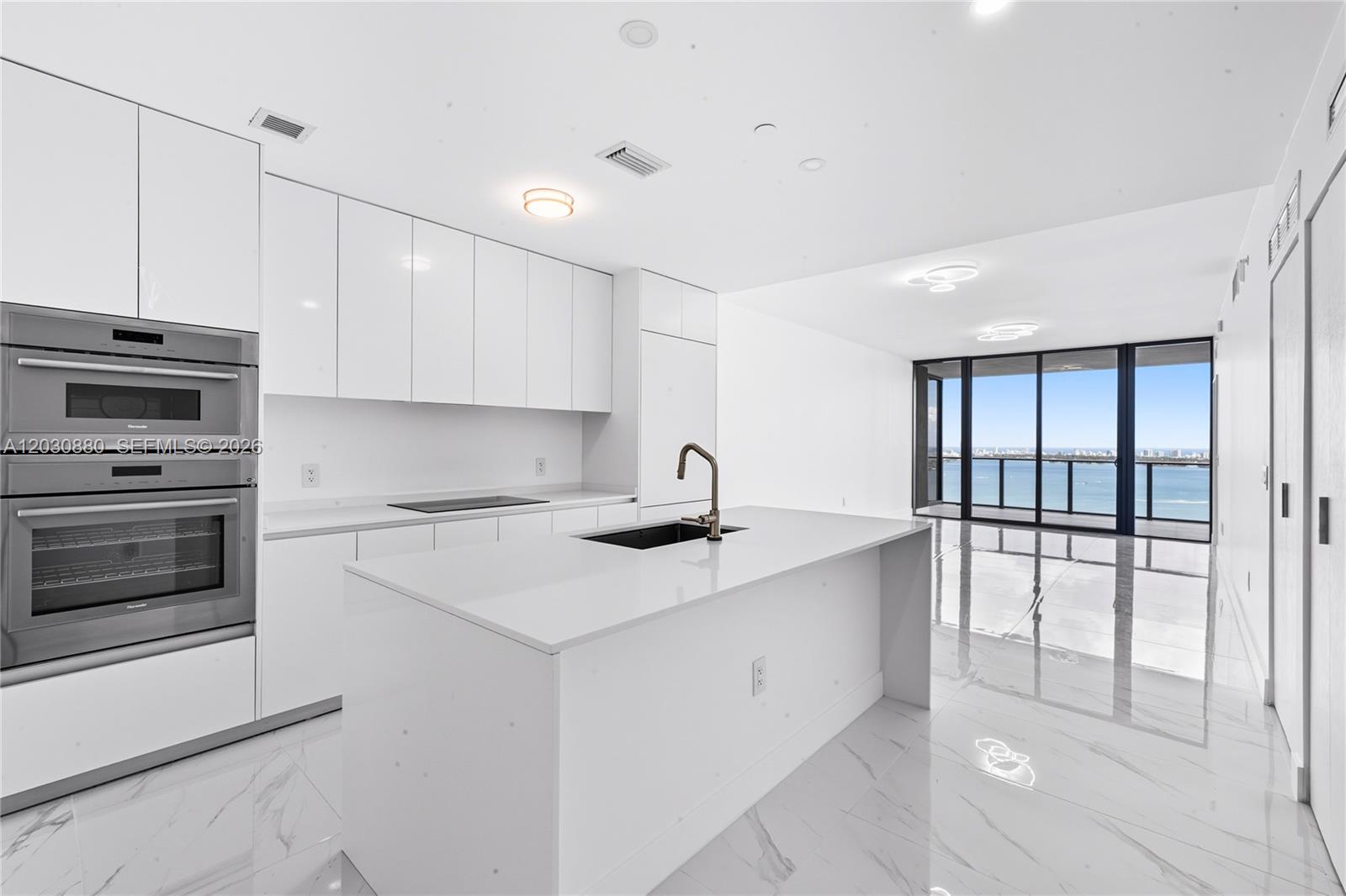 A modern white kitchen features a central island, stainless steel appliances, and floor-to-ceiling windows — 700 NE 24th St # 3502, Miami FL 33137, MIAMI, FL