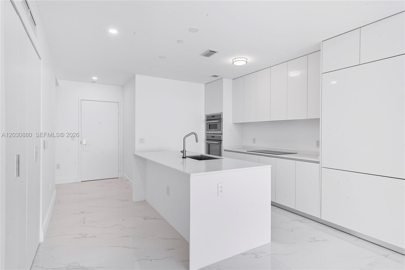 A modern white kitchen features a central island, sleek cabinetry, and marble-patterned tile flooring — 700 NE 24th St # 3502, Miami FL 33137, MIAMI, FL