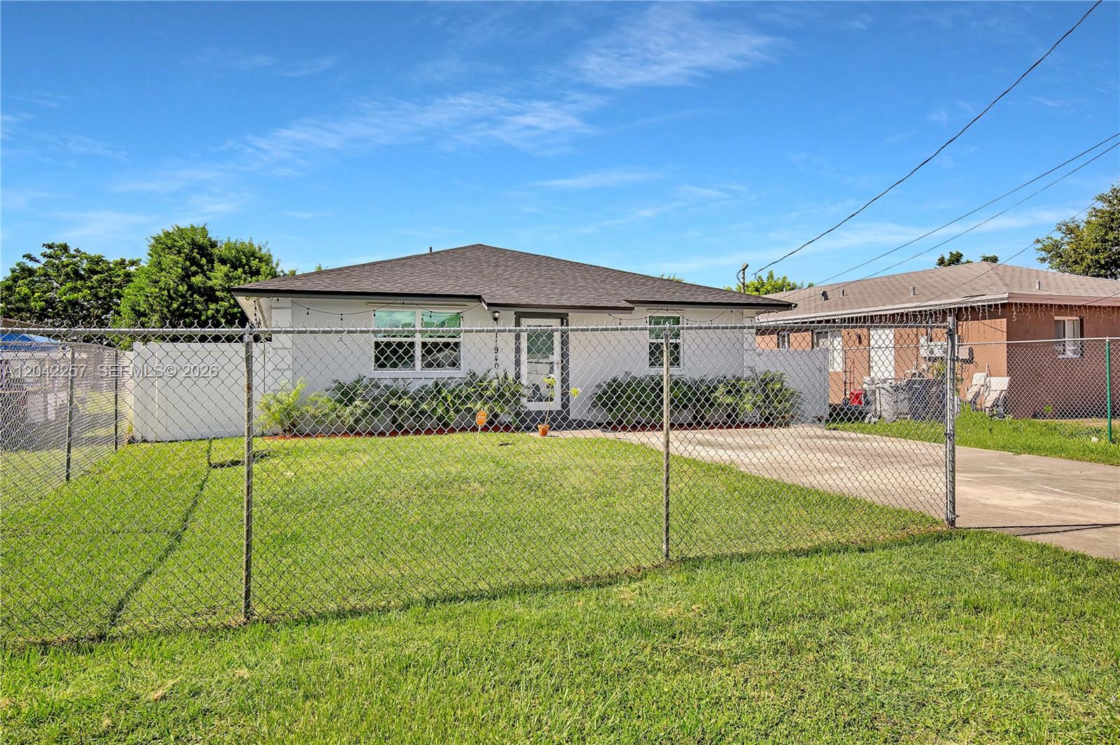 A single-story house with a white exterior and a dark roof sits behind a chain-link fence — 11940 SW 212th St, Miami FL 33177, MIAMI, FL
