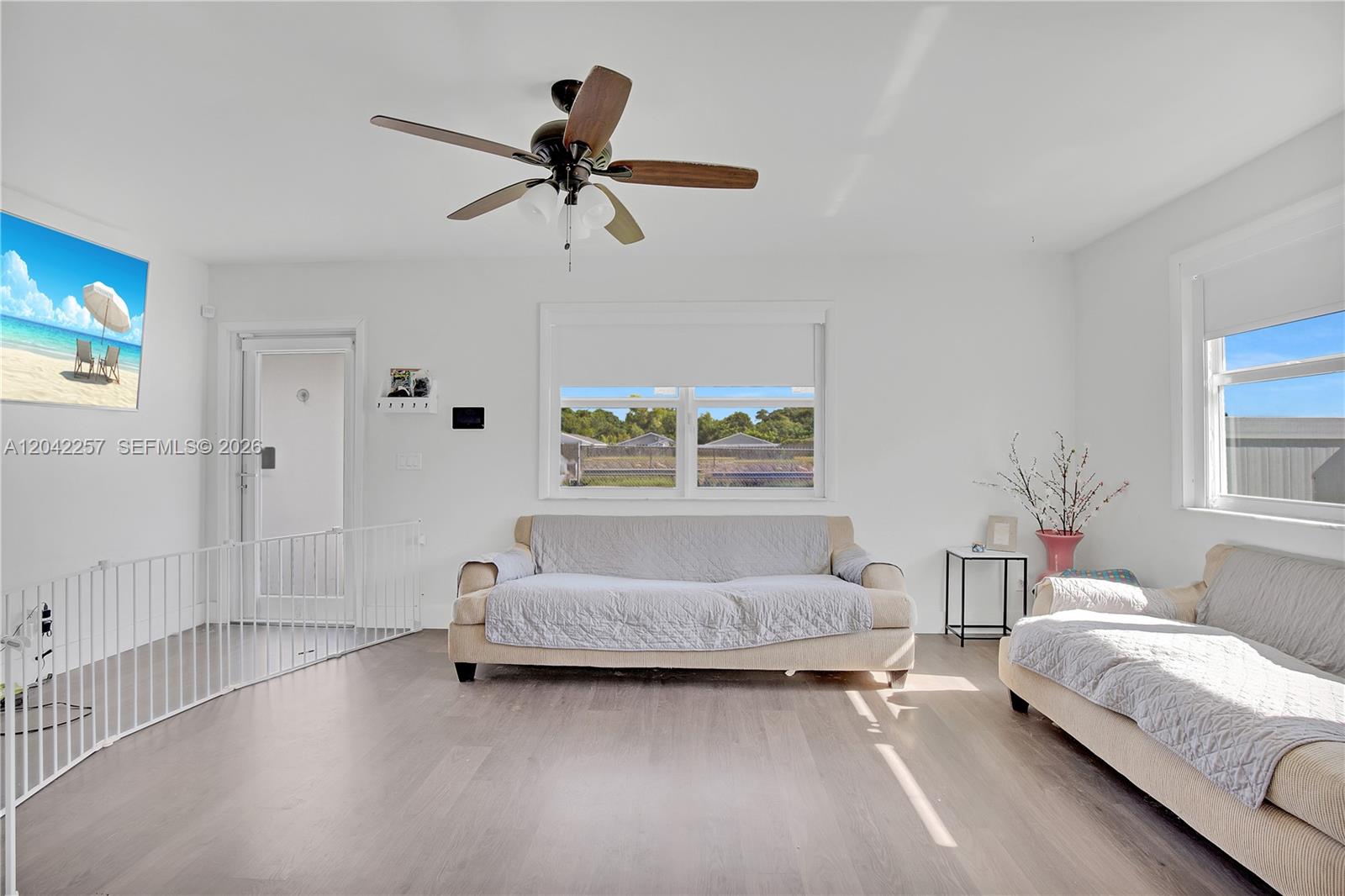 A bright living room features light wood floors, two sofas, a ceiling fan, and windows — 11940 SW 212th St, Miami FL 33177, MIAMI, FL