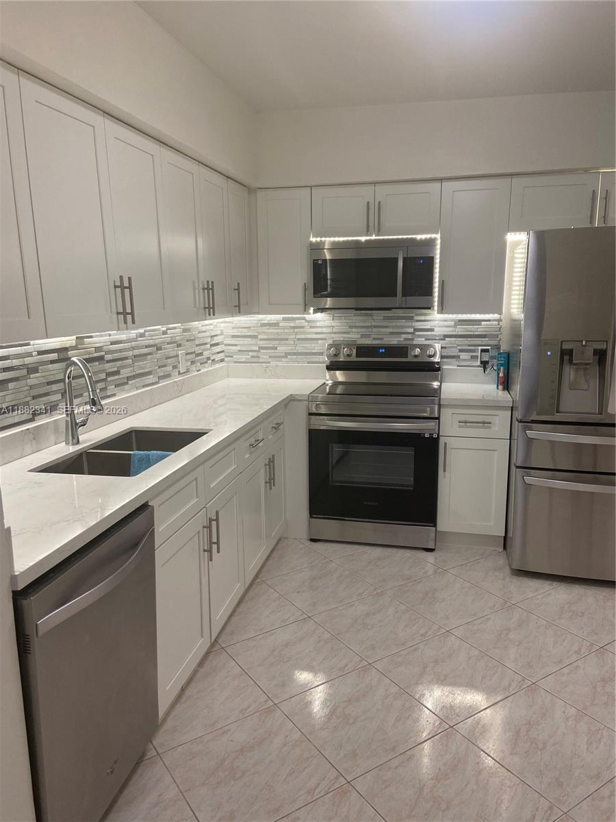 A kitchen features white shaker cabinets, stainless steel appliances, and a tiled backsplash — 1301 NE 7th St # 106, Hallandale Beach FL 33009, HALLANDALE BEACH, FL