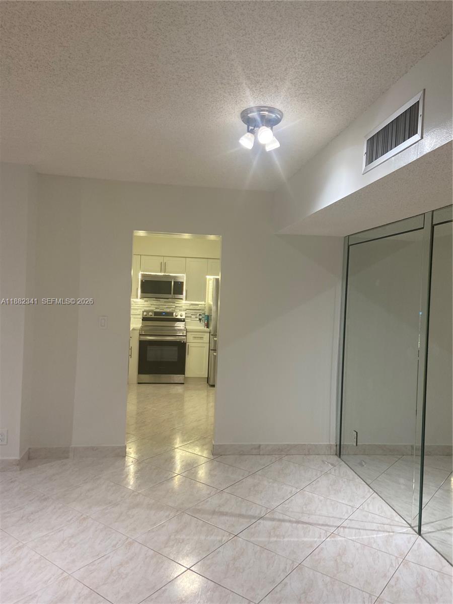 A tiled room leads into a kitchen featuring stainless steel appliances and white cabinetry — 1301 NE 7th St # 106, Hallandale Beach FL 33009, HALLANDALE BEACH, FL