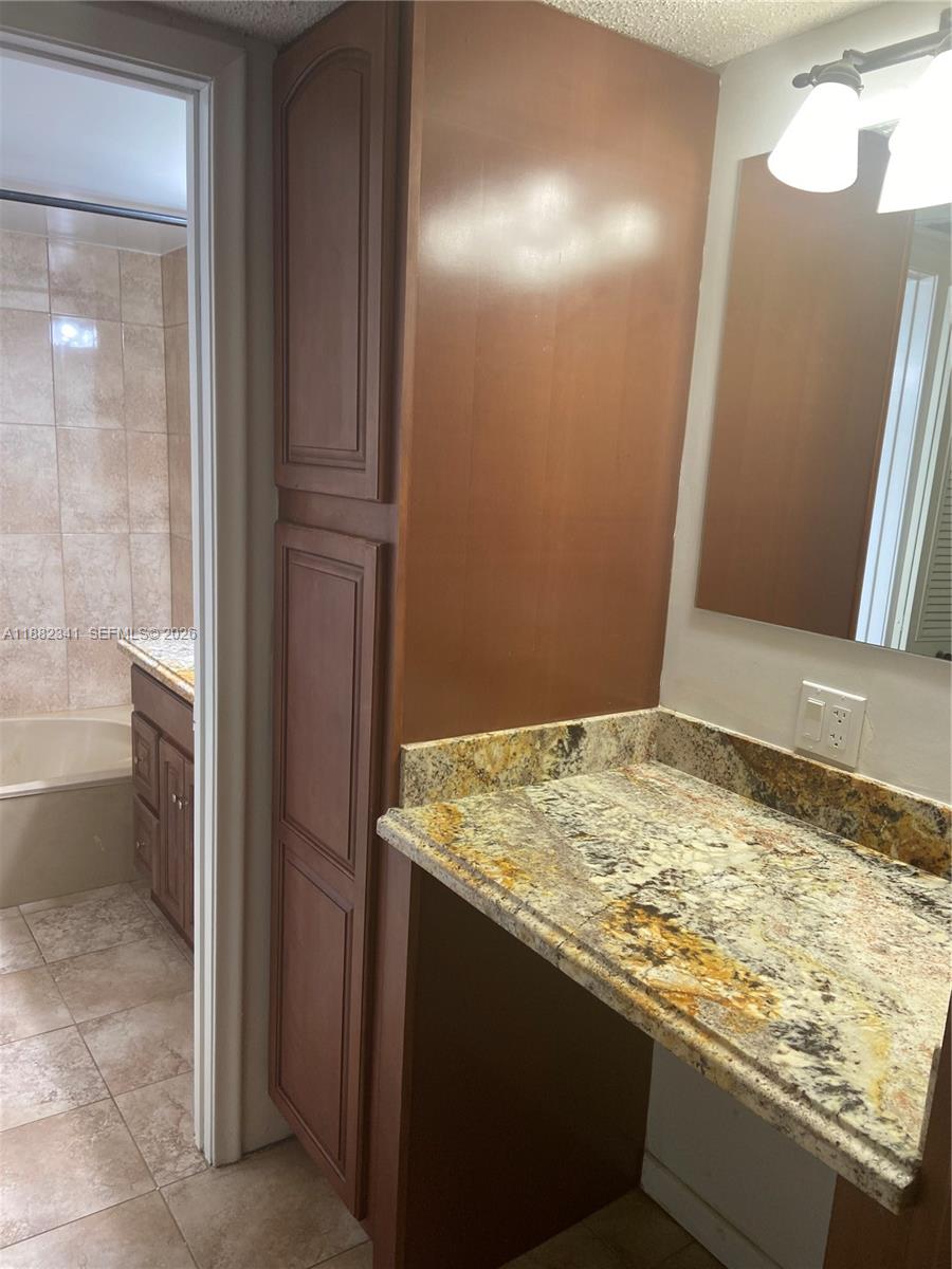 A bathroom features a granite vanity countertop, a tall wooden cabinet, and a tiled shower — 1301 NE 7th St # 106, Hallandale Beach FL 33009, HALLANDALE BEACH, FL