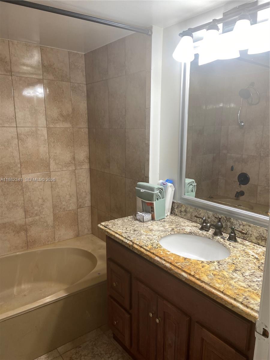 A bathroom features a granite vanity, a dark wood cabinet, and a tiled tub surround — 1301 NE 7th St # 106, Hallandale Beach FL 33009, HALLANDALE BEACH, FL