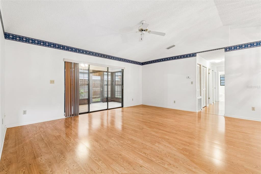 A spacious living room with light wood flooring, white walls, blue wallpaper border, and sliding doors — 11301 MAYBROOK AVENUE, RIVERVIEW, FL