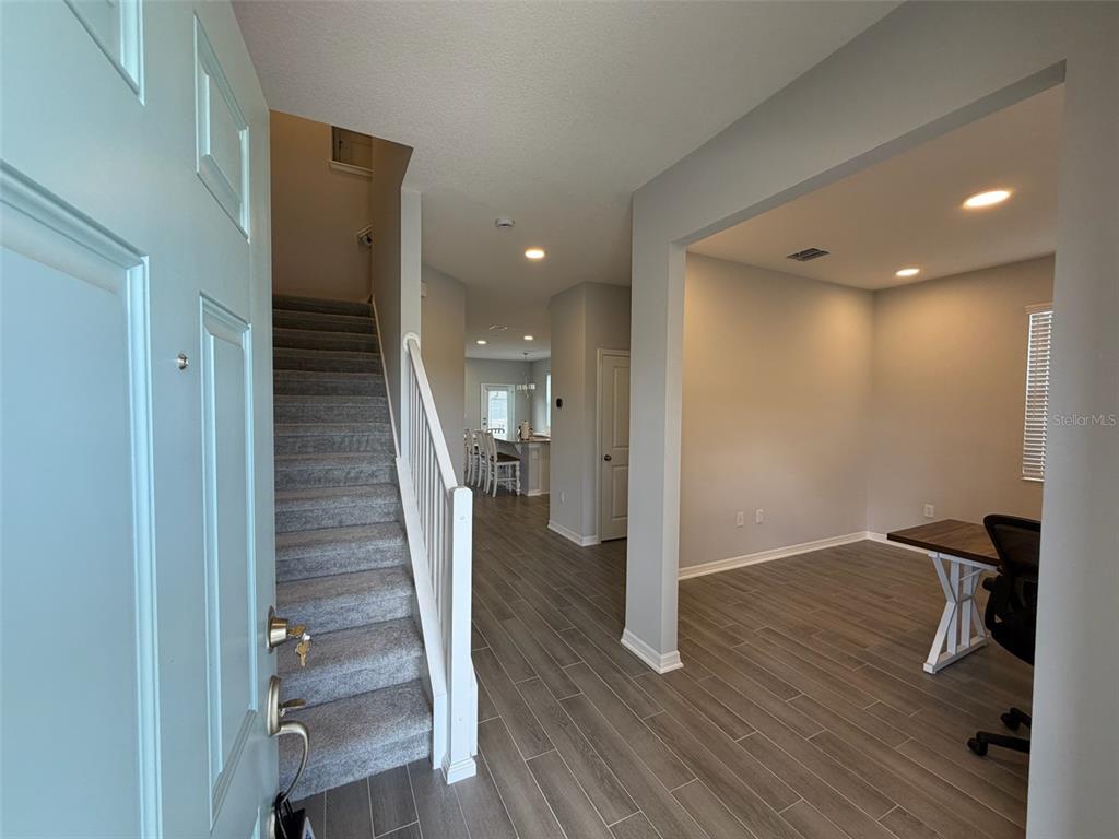 An entryway with gray wood-look tile floors leads to a carpeted staircase and office space — 15935 GRAFTON WAY, WINTER GARDEN, FL