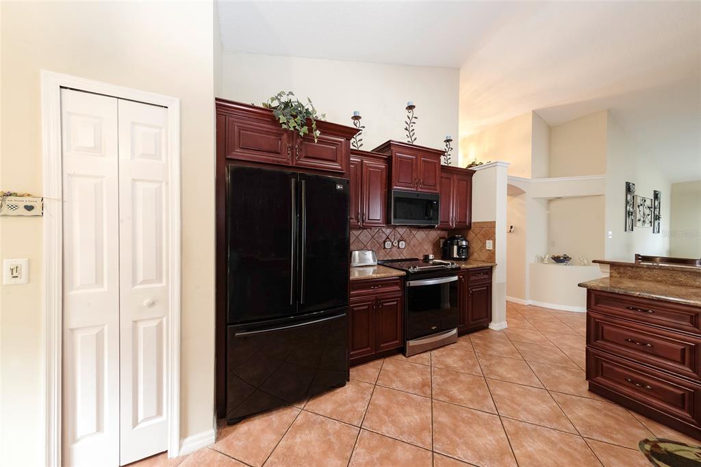 A kitchen features dark wood cabinets, black appliances, granite countertops, and light-colored tile flooring — 2679 ALAMOSA PLACE, LAKE MARY, FL