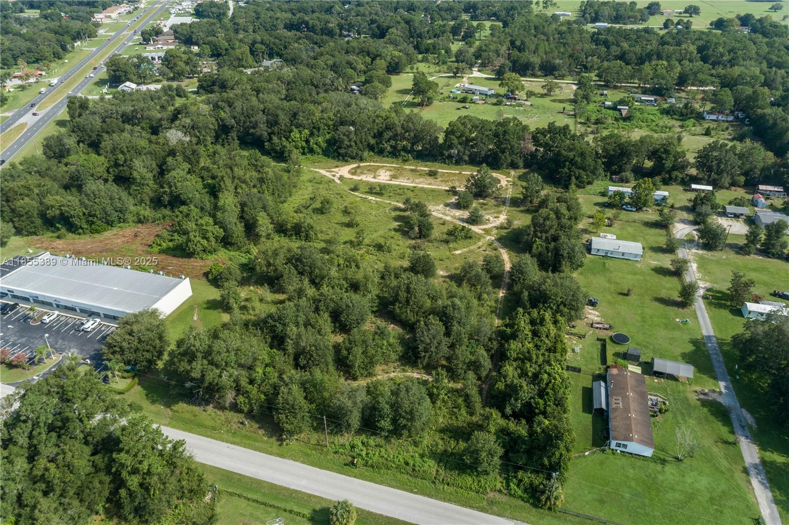 An aerial view shows a large, partially wooded vacant lot adjacent to a commercial building — 7711 SE 126th Place, Ocala FL 34420, OCALA, FL