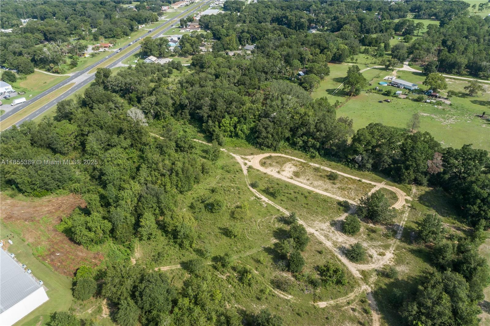 An aerial view shows a large, undeveloped grassy lot with dirt paths and surrounding trees — 7711 SE 126th Place, Ocala FL 34420, OCALA, FL