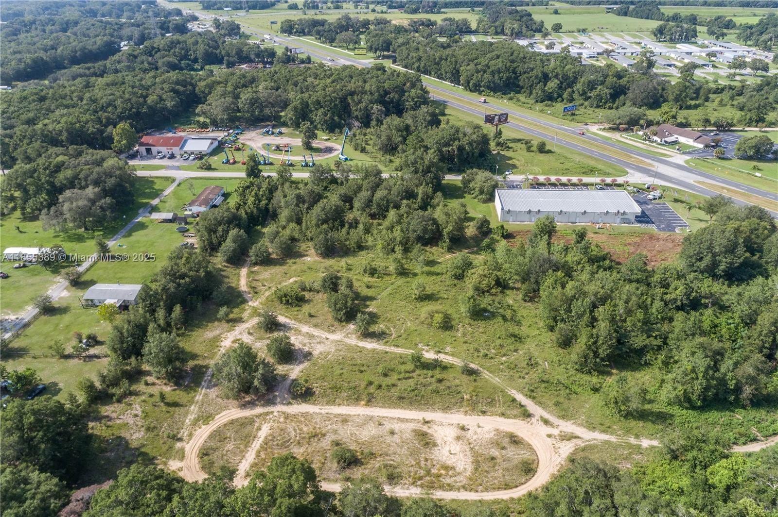 An aerial view shows a large, partially cleared grassy lot with dirt tracks and surrounding trees — 7711 SE 126th Place, Ocala FL 34420, OCALA, FL