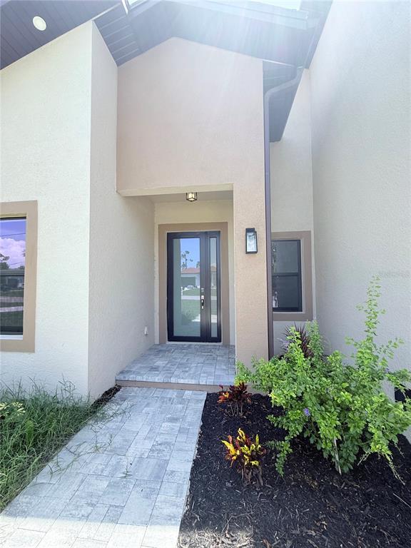 A modern home entrance features a glass-paneled front door, a paved walkway, and landscaping — 273 ANTIS DRIVE, ROTONDA WEST, FL