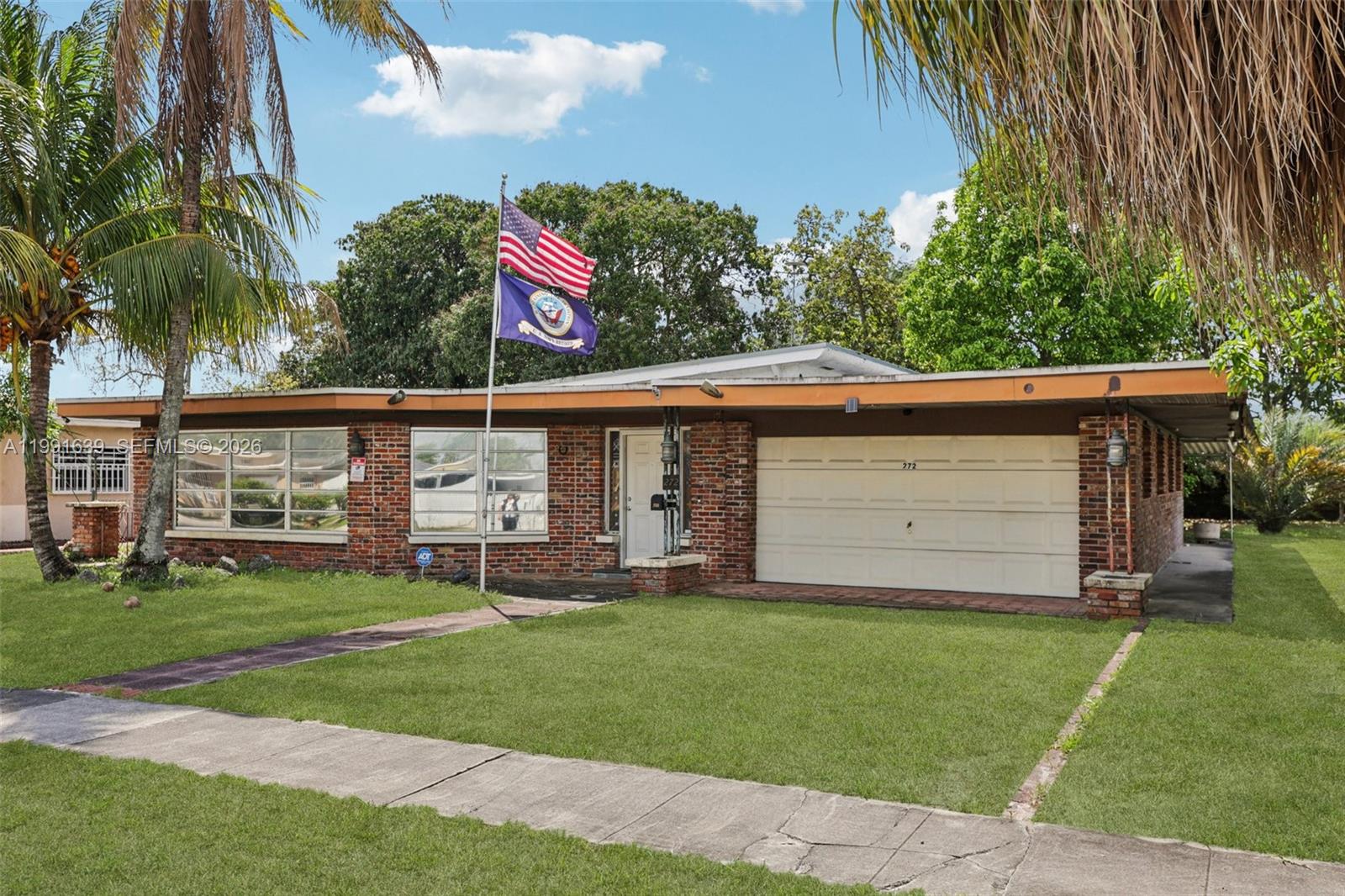 A single-story brick house features a garage, a front lawn, and an American flag — 272 W 46th St, Hialeah FL 33012, HIALEAH, FL