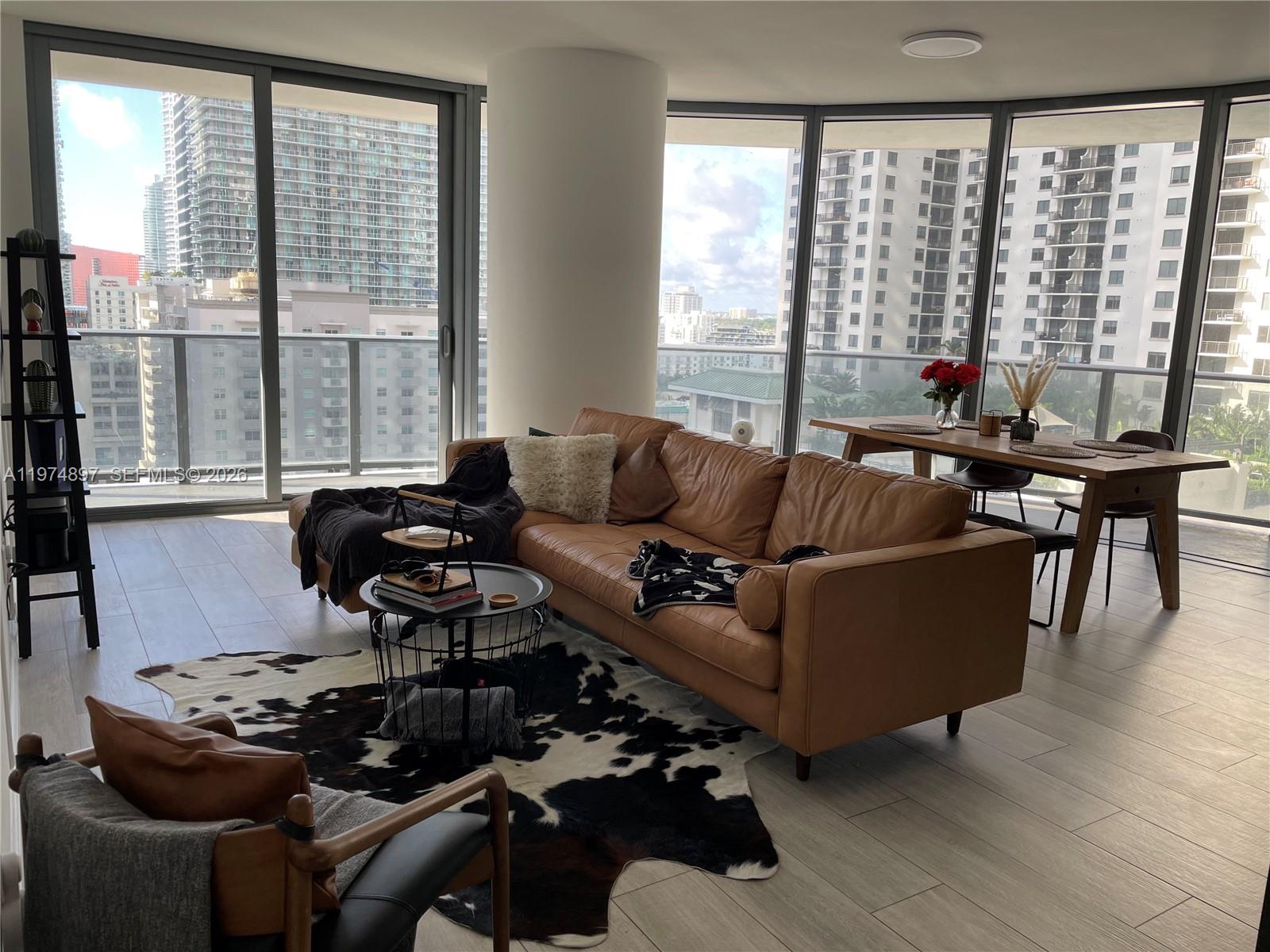 A living and dining area features a leather sofa, cowhide rug, and floor-to-ceiling windows — 45 SW 9th St # 1206, Miami FL 33130, MIAMI, FL