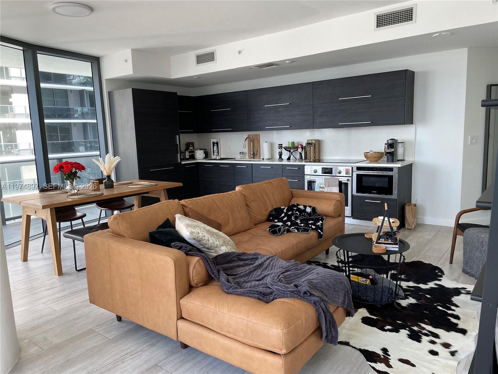 An open-concept living area features a tan leather sectional, dining table, and dark kitchen cabinetry — 45 SW 9th St # 1206, Miami FL 33130, MIAMI, FL