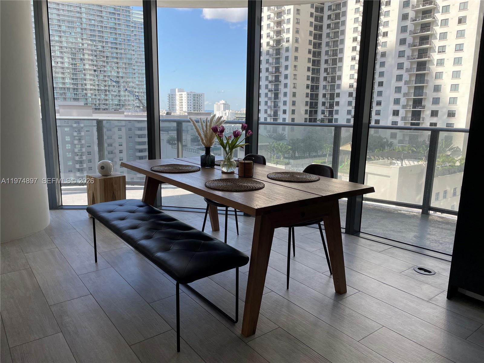 A dining area features a wooden table, a black tufted bench, and floor-to-ceiling windows — 45 SW 9th St # 1206, Miami FL 33130, MIAMI, FL