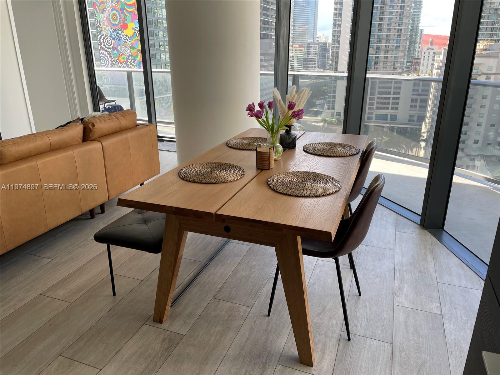 A dining area features a wooden table with four placemats and city views through windows — 45 SW 9th St # 1206, Miami FL 33130, MIAMI, FL