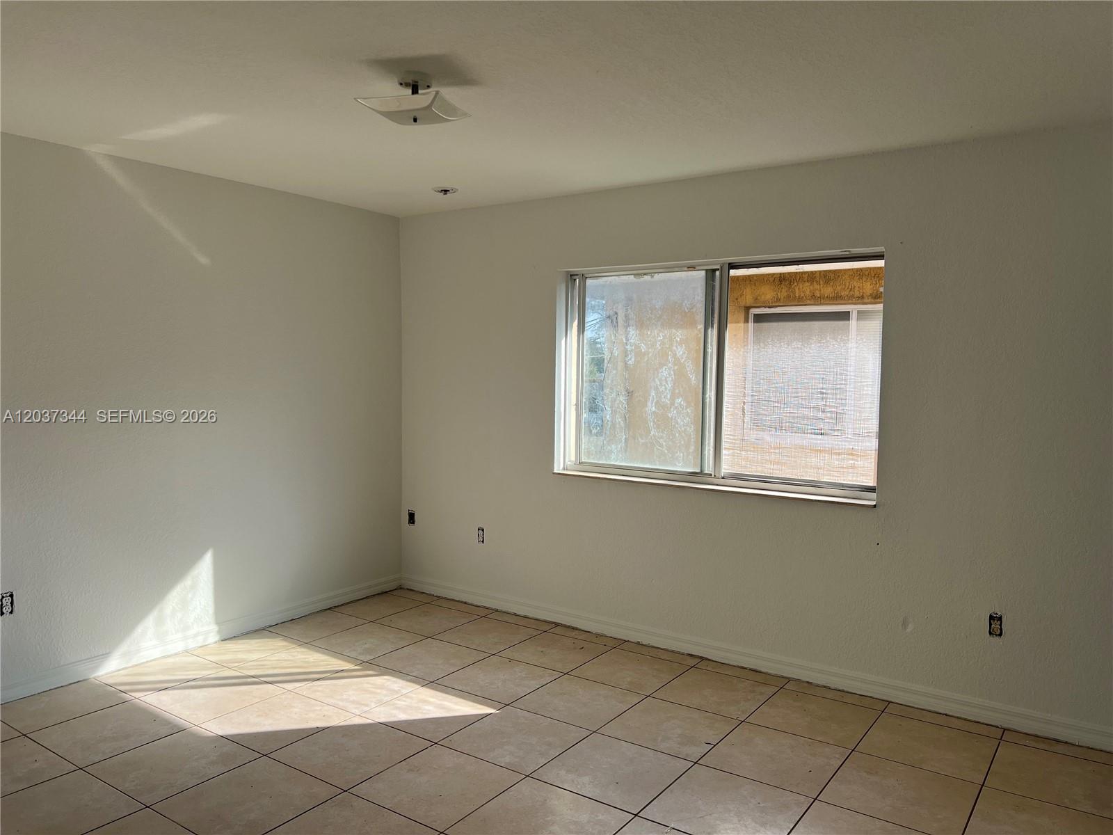 An empty room features white walls, beige tile flooring, and a single window — 7012 NW 6th Ct # 7012, Miami FL 33150, MIAMI, FL
