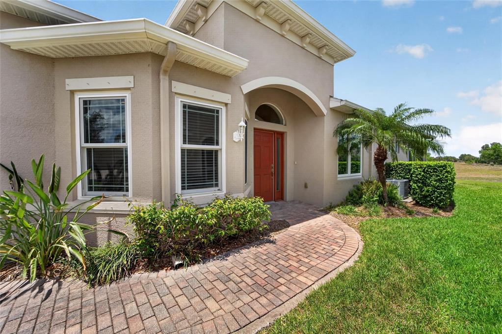 A tan house exterior features a red front door, arched entryway, and brick paver walkway — 642 CHIPPER DRIVE, SUN CITY CENTER, FL