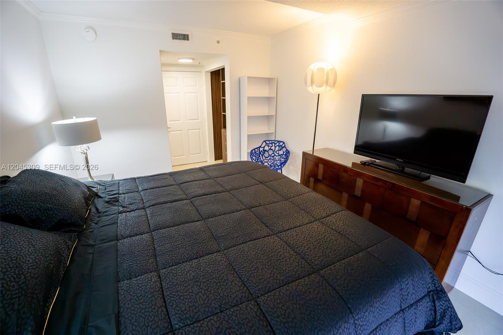A bedroom features a dark bedspread, a wooden dresser with a television, and a floor lamp — 2951 S Bayshore Dr # 716, Miami FL 33133, MIAMI, FL