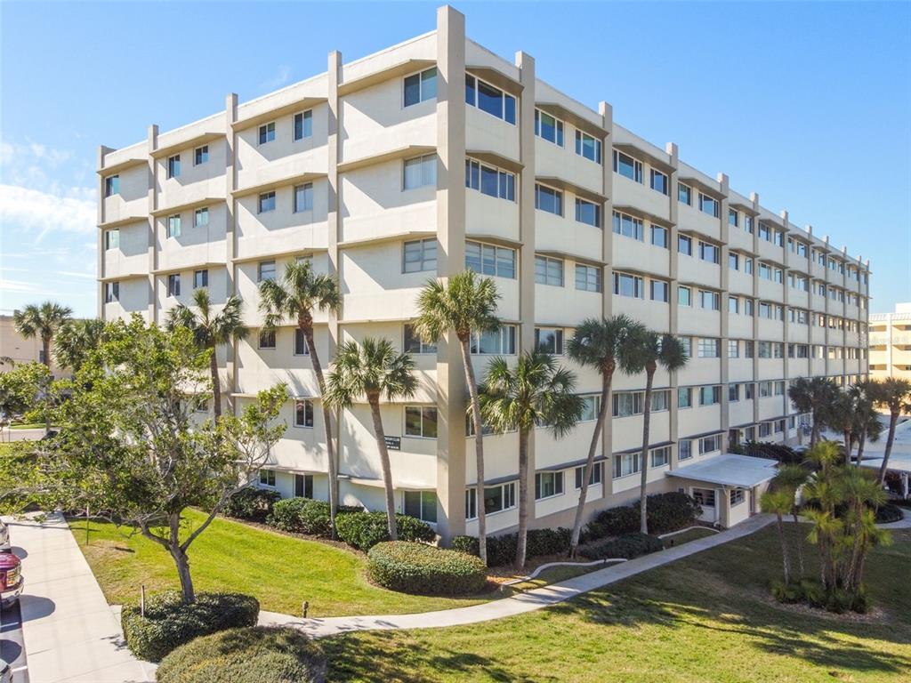 An exterior view of a multi-story apartment building with palm trees and a landscaped lawn — 100 BLUFF VIEW DRIVE UNIT 607A, BELLEAIR BLUFFS, FL