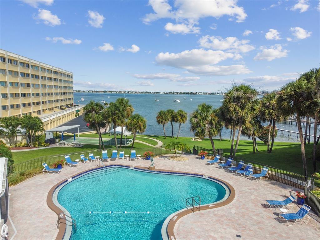 An elevated view of a swimming pool, palm trees, and a building overlooking the water — 100 BLUFF VIEW DRIVE UNIT 607A, BELLEAIR BLUFFS, FL