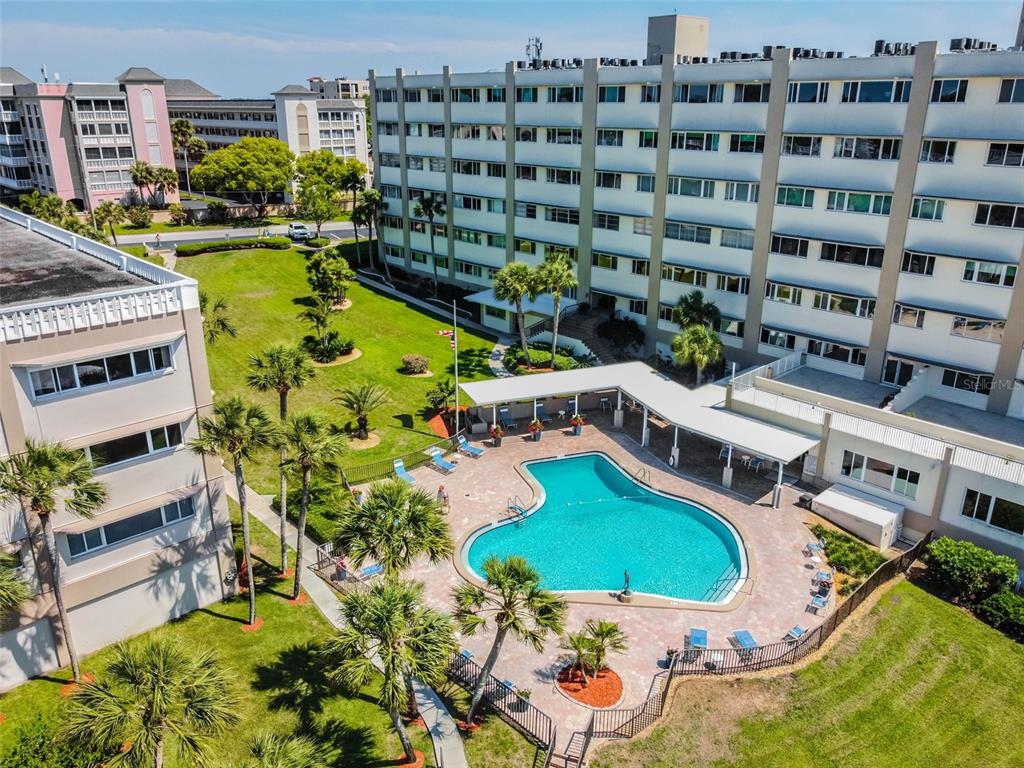 An aerial view of a swimming pool area surrounded by palm trees and multi-story apartment buildings — 100 BLUFF VIEW DRIVE UNIT 607A, BELLEAIR BLUFFS, FL