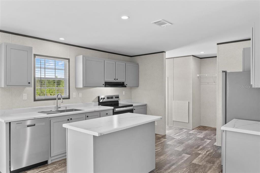 A kitchen features gray cabinets, white countertops, a center island, and stainless steel appliances — 2436 EDWIN STREET NE, WINTER HAVEN, FL