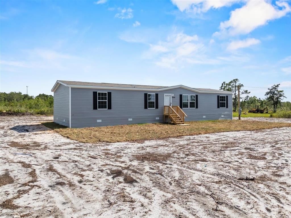 A single-story manufactured home with grey siding sits on a sandy, undeveloped lot — 2436 EDWIN STREET NE, WINTER HAVEN, FL