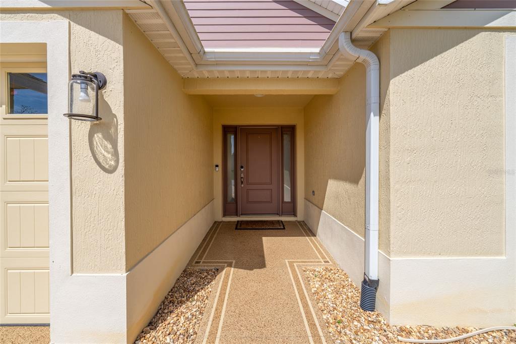 A covered entryway features a brown front door with sidelights and a textured walkway — 4537 BROOKE LANE, THE VILLAGES, FL