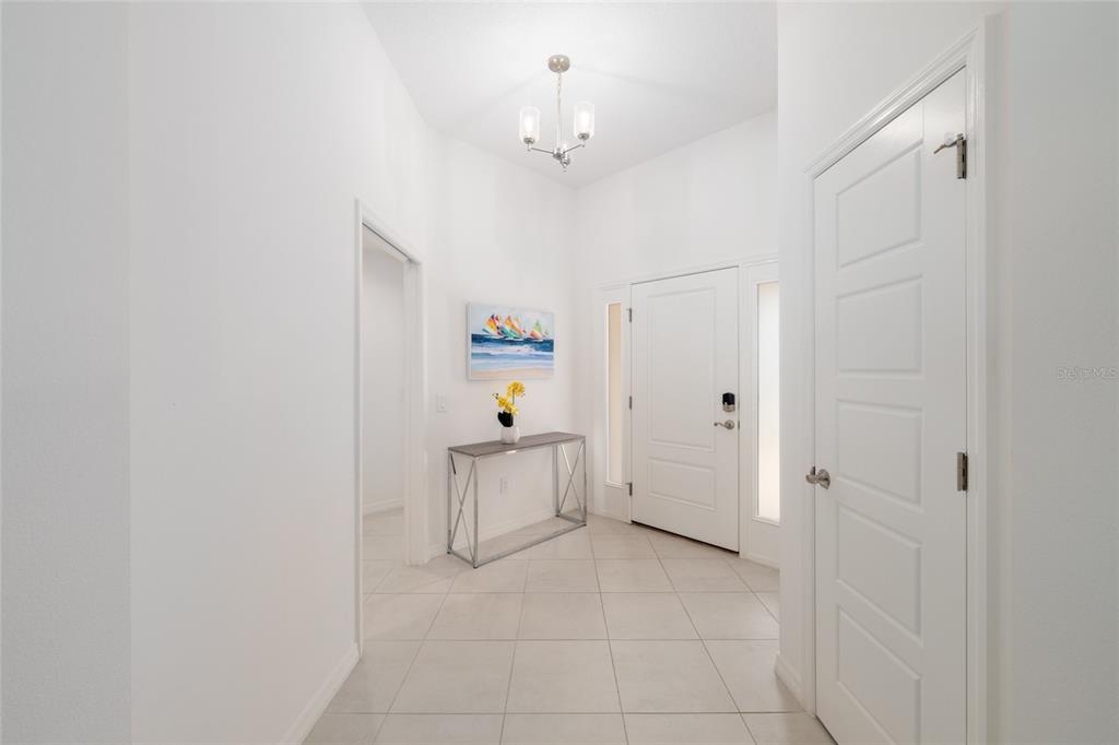 A bright entryway features white walls, tiled floors, a console table, and a chandelier — 4537 BROOKE LANE, THE VILLAGES, FL