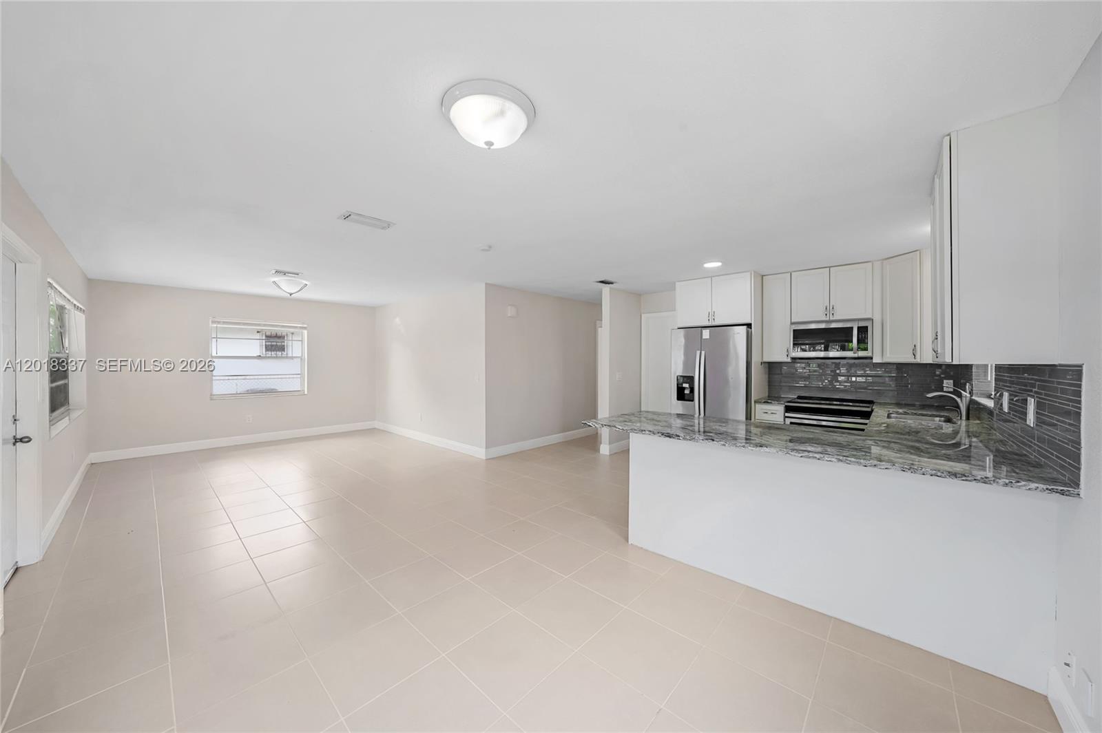 An open-concept kitchen and living area features light tile flooring and white cabinetry — 429 Avenida Hermosa, West Palm Beach FL 33405, WEST PALM BEACH, FL