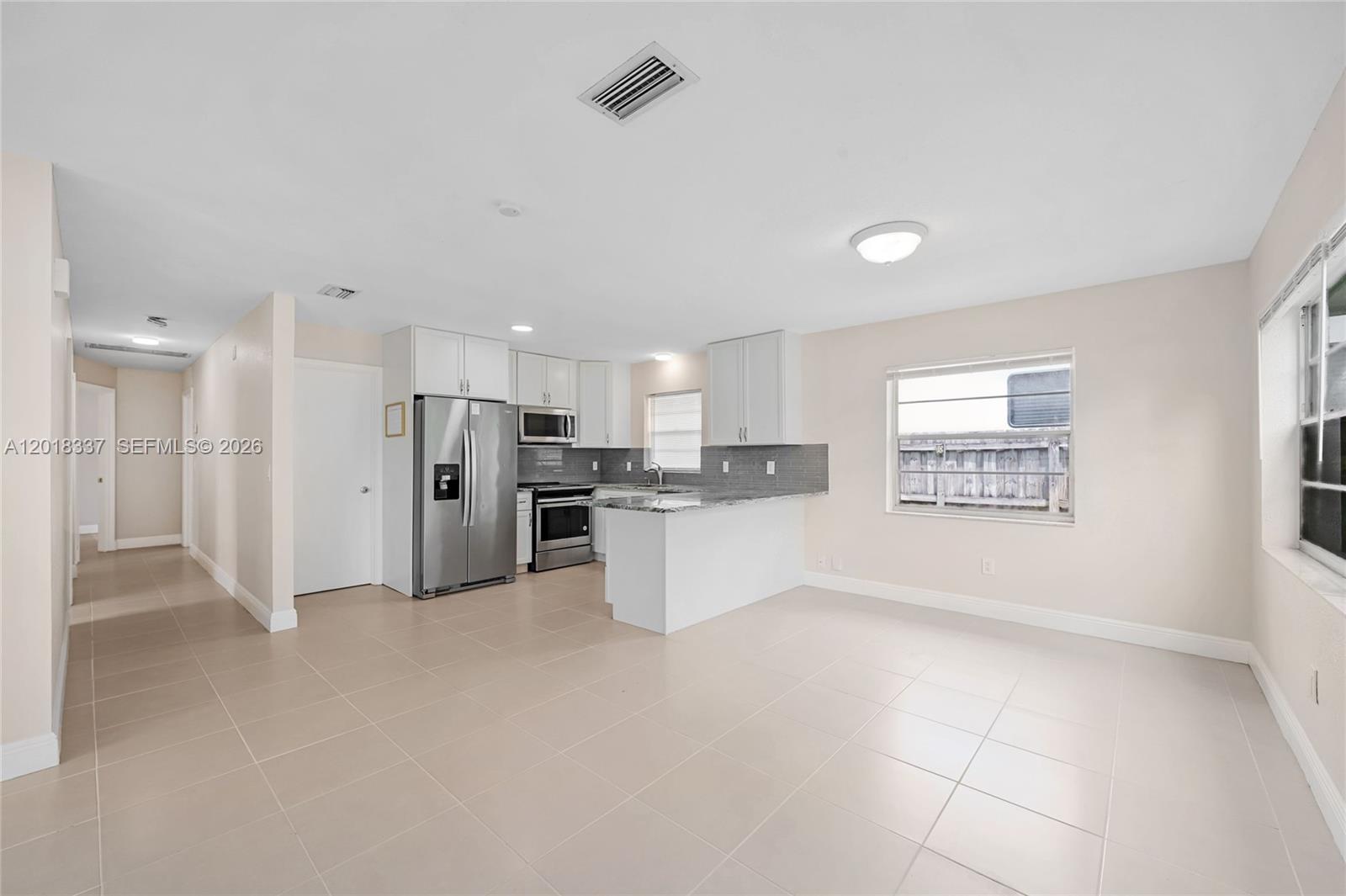 A kitchen with white cabinets, stainless steel appliances, and tile flooring opens to a dining area — 429 Avenida Hermosa, West Palm Beach FL 33405, WEST PALM BEACH, FL